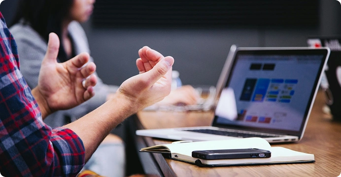 Hands gesturing in a meeting beside a laptop and notebook