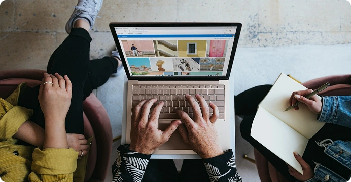 Hands typing on a laptop showing a website design while another person takes notes
