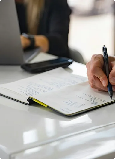 A hand writing in an open notebook on a white desk