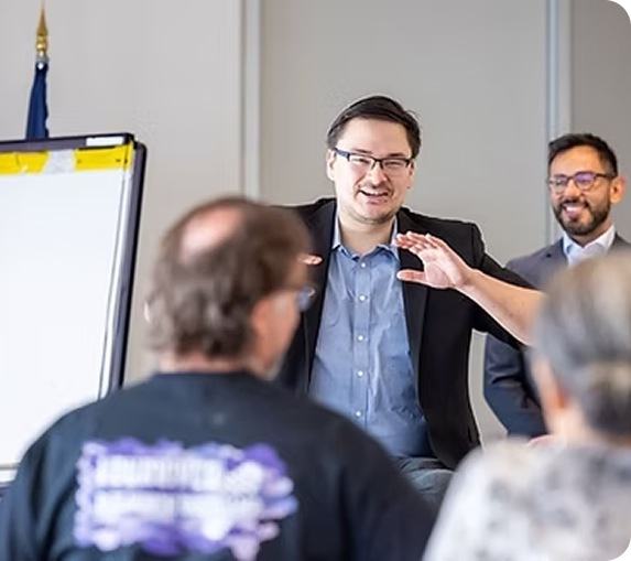A speaker smiling and gesturing to an audience at a small-business support program session